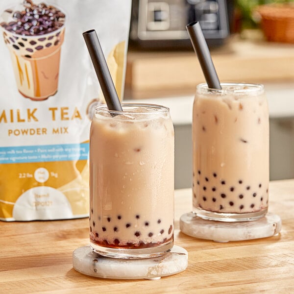 Two glasses of milk tea with brown liquid and straws on a table.