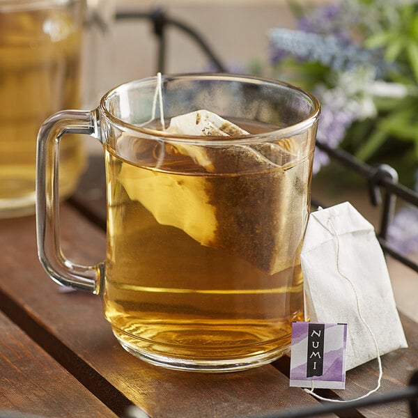 A glass mug of Numi Organic Sweet Slumber tea with a tea bag on a table.