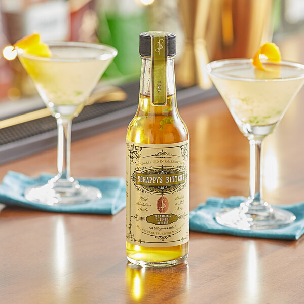 A bottle of Scrappy's Lime Bitters on a table next to a glass of liquid.