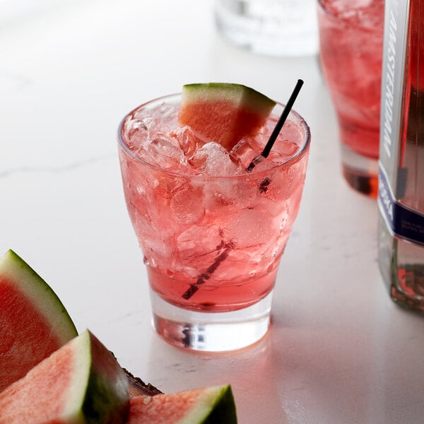 A glass of Monin watermelon flavoring syrup with a watermelon slice on the rim.