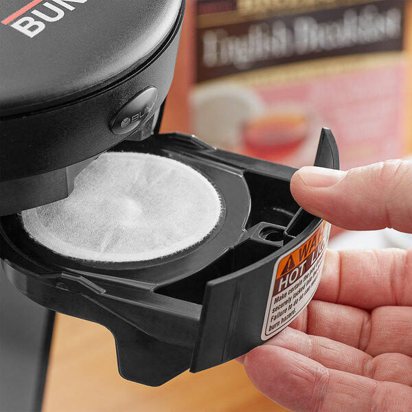 A hand holding a black container of Bigelow English Breakfast Tea single serve pods.