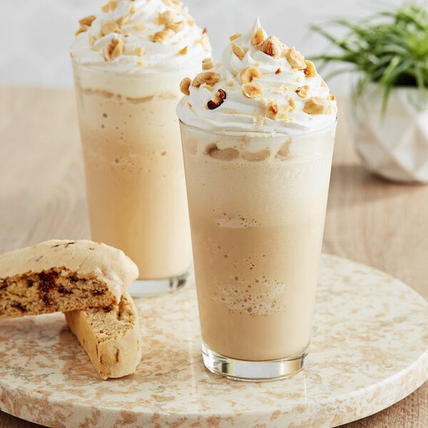 Two glasses of The Frozen Bean Double Shot Hazelnut Latte Blended Ice Coffee with whipped cream and nuts on top.