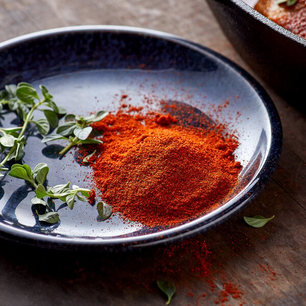 A plate with a pile of red powder and green leaves with a bowl of red powder.