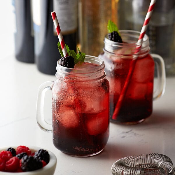 Two mason jars filled with red drinks and straws on a table in a cocktail bar.