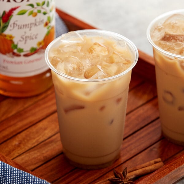 A cup of iced coffee with a bottle of Monin Pumpkin Spice syrup on a table.
