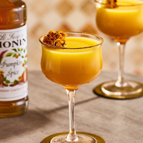A glass of pumpkin spice-flavored beverage garnished with a flower, next to a bottle of Monin Premium Pumpkin Spice Flavoring Syrup.