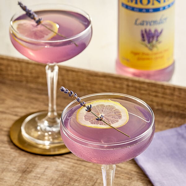 Two glasses of pink and purple lavender-flavored drinks with lemon slices and lavender on top.