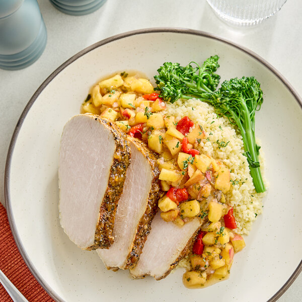 A plate with sliced pork loin topped with a peach salsa, served with couscous and broccolini.