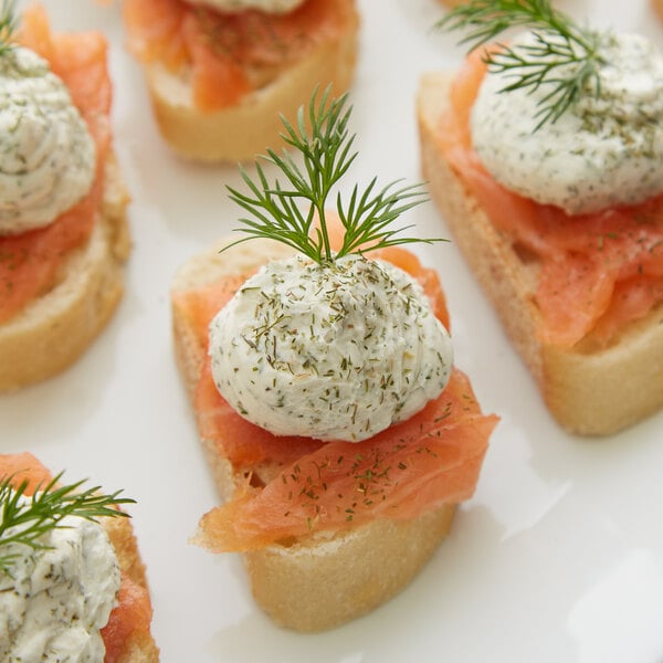 A plate of small sandwiches topped with cream cheese and Regal Dill Weed.