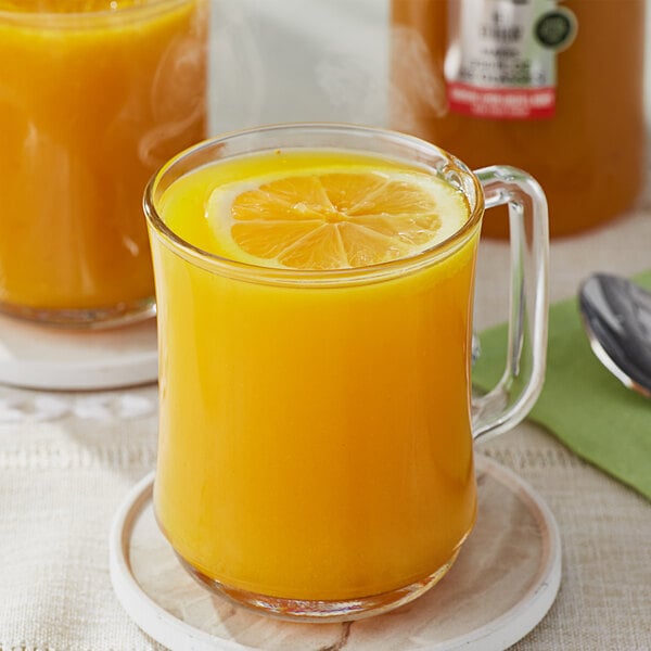 A glass mug of orange liquid with a lemon slice in it.