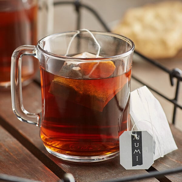 A glass mug of Numi Organic Emperor's Pu-Erh Tea with a tea bag in it on a white tray.