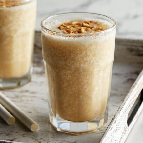 A glass of milkshake with a brown liquid and nuts next to a bottle of DaVinci Gourmet Classic Peanut Butter Flavoring Syrup.