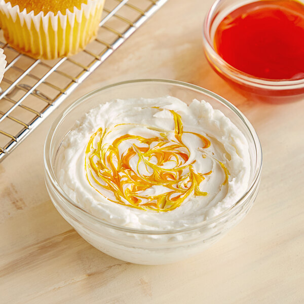 A bowl of yogurt with a swirl of yellow liquid and a cupcake.