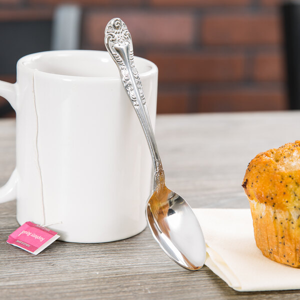 A Oneida Rosewood stainless steel teaspoon next to a white mug of tea on a table.