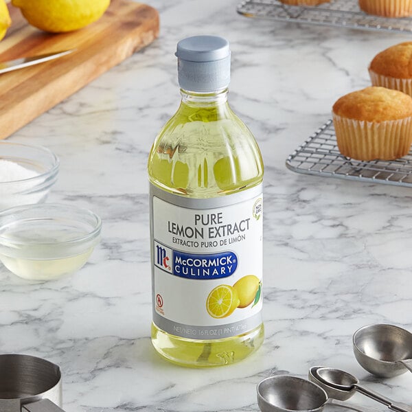 A bottle of McCormick Pure Lemon Extract on a counter next to muffins.