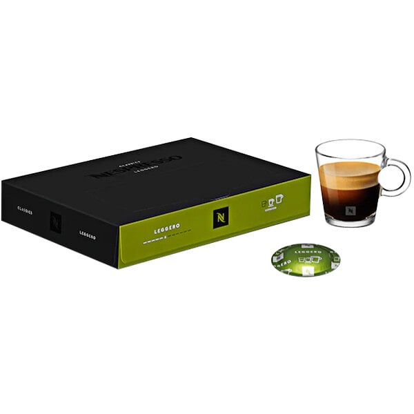 A black Nespresso box with a green lid on a table with a glass of brown Nespresso coffee.