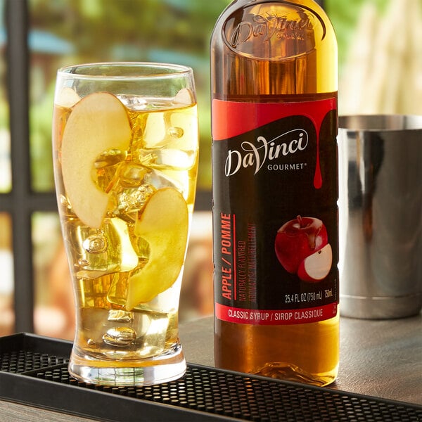 A glass of apple cider and a bottle of DaVinci Gourmet Classic Apple Flavoring on a table in a cocktail bar.