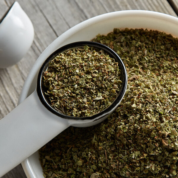 A white measuring cup with a pile of Regal marjoram leaves.