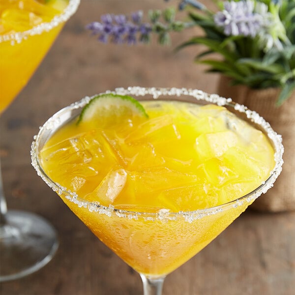 A yellow drink with ice and lime in a martini glass with a sugar rim and a lime slice.