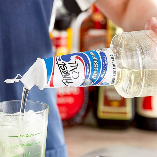 A person pouring Finest Call Premium Lite Simple Syrup into a glass of ice.
