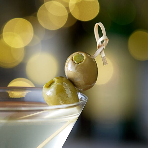 A martini with a green olive stuffed with a dill pickle on a table in a cocktail bar.
