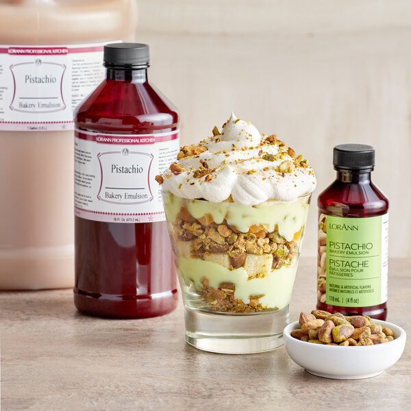 A dessert in a glass with a bottle of LorAnn Oils Pistachio Bakery Emulsion on a table with a bowl of pistachios.