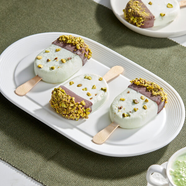 A plate of pistachio-flavored ice cream bars partially dipped in chocolate and sprinkled with chopped pistachios.