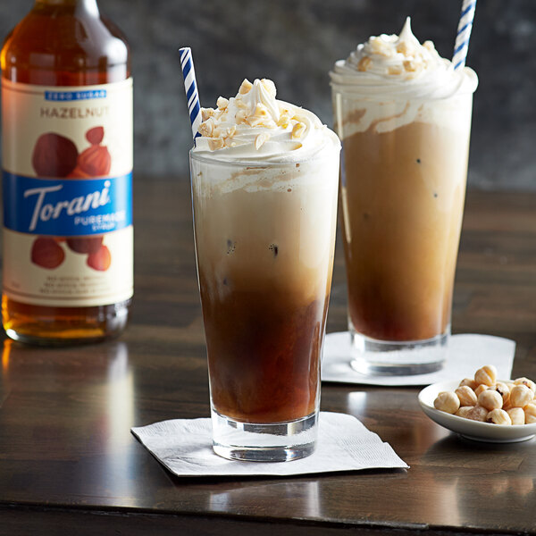 Two glasses of iced coffee with whipped cream and hazelnuts using Torani Puremade Zero Sugar Hazelnut Flavoring Syrup.