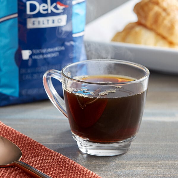 A glass cup of Lavazza Dek Filtro decaf coffee with steam on a table.