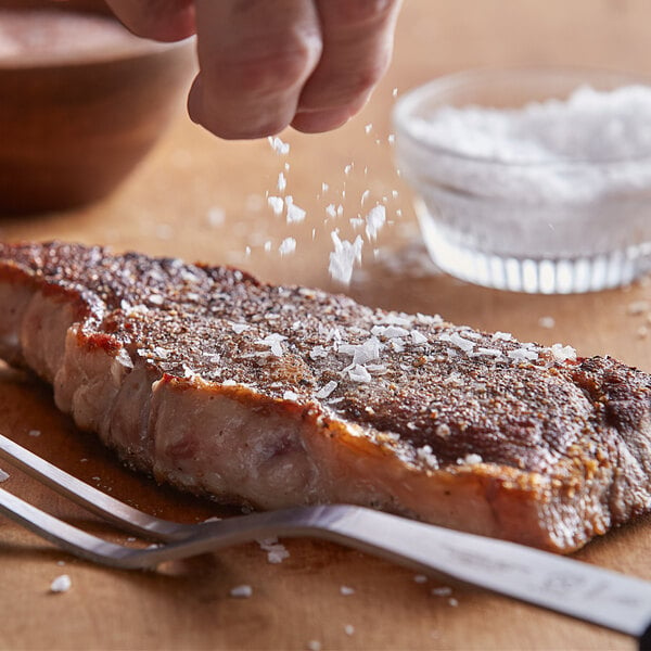 A hand sprinkling Regal Spanish sea salt flakes on a piece of meat.