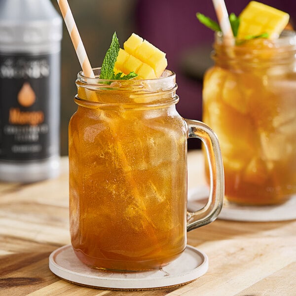 A mason jar filled with iced tea garnished with mango chunks and mint, served with a straw.