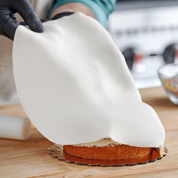 A person using Satin Ice white rolled fondant to cover a cake.