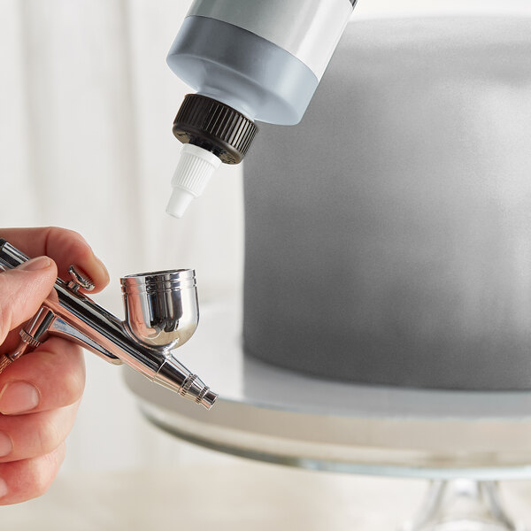 A person using Chefmaster Metallic Silver Airbrush Color to spray a cake using a silver airbrush.