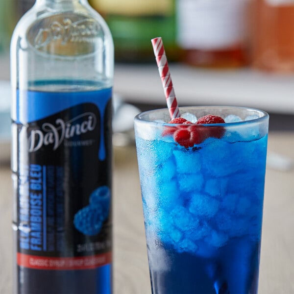 A blue drink with ice and a raspberry in a glass next to a bottle of DaVinci Gourmet Classic Blue Raspberry Flavoring Syrup.