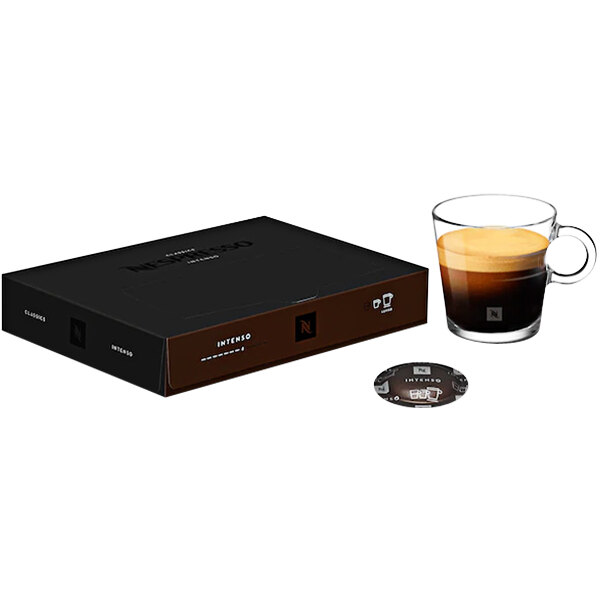 A black Nespresso box with a brown lid on a table next to a glass of coffee.