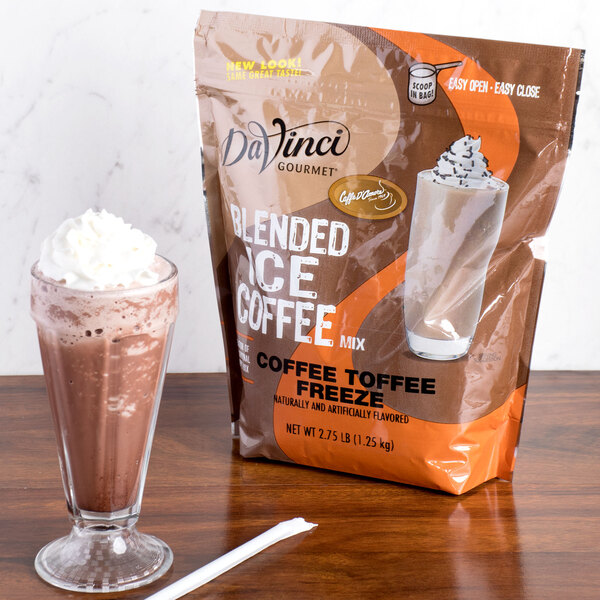 A glass of coffee with whipped cream next to a bag of DaVinci Gourmet Coffee Toffee Freeze Mix.