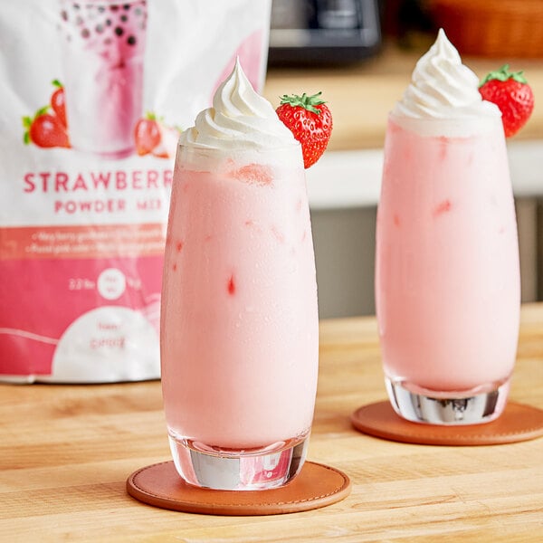 Two glasses of pink strawberry milkshakes with strawberries on top.