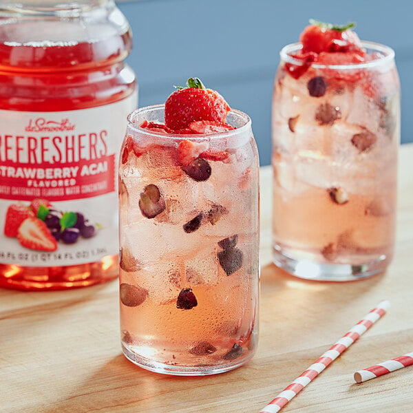 A glass of Dr. Smoothie strawberry acai refresher with berries and a straw.