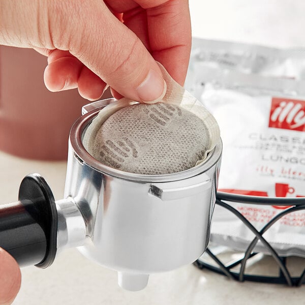 A hand using an illy coffee filter to make coffee.