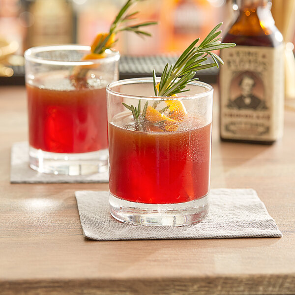 Two glasses of red drinks garnished with rosemary on a table with King Floyd's Barrel Aged Aromatic Bitters.