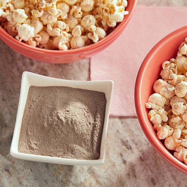 A white bowl of popcorn with brown powder next to a white bowl of brown powder.