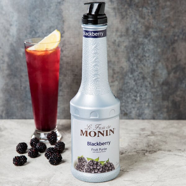 A white Monin bottle of blackberry fruit puree next to a glass of red liquid.