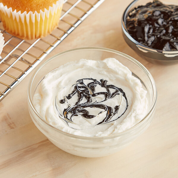 A bowl of white frosting with a swirl of black Chefmaster Coal Black gel food coloring on a cupcake.