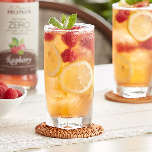 A glass of lemonade with raspberries and mint next to a bottle of Monin Zero Calorie Natural Raspberry Flavoring Syrup.