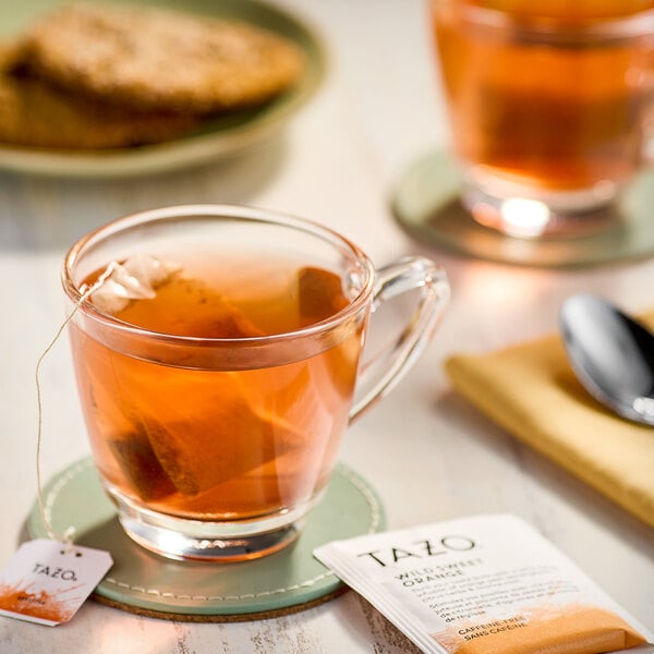 A glass cup of Tazo Wild Sweet Orange tea with a tea bag in it on a table.