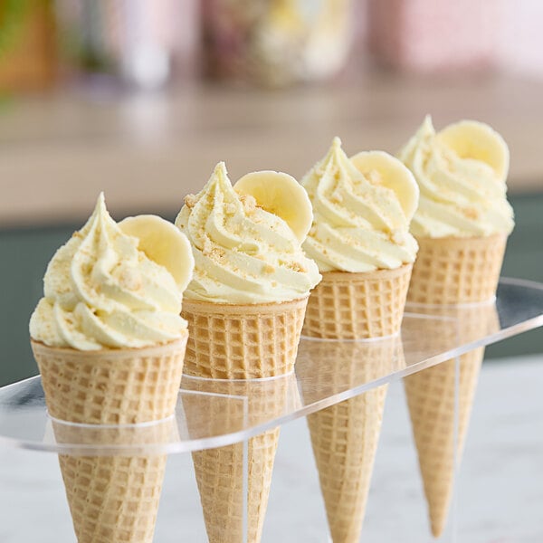 Three waffle ice cream cones with yellow ice cream and bananas on top.