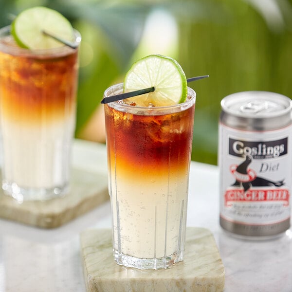 A glass of Goslings Diet Ginger Beer with ice and a lime wedge on a white table.
