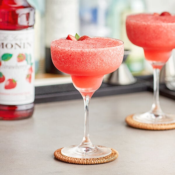 Two glasses of pink drinks made with Monin strawberry syrup on a bar table.