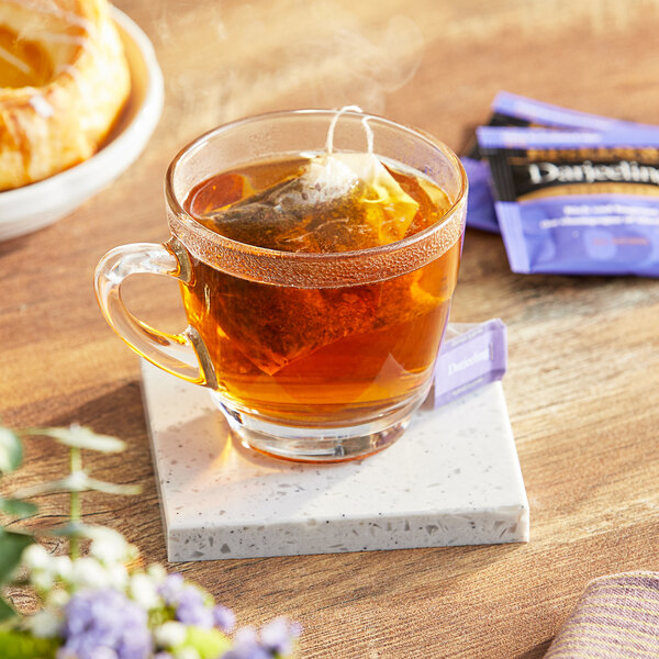 A glass cup of Bigelow Darjeeling tea on a marble coaster with a tea bag in it.