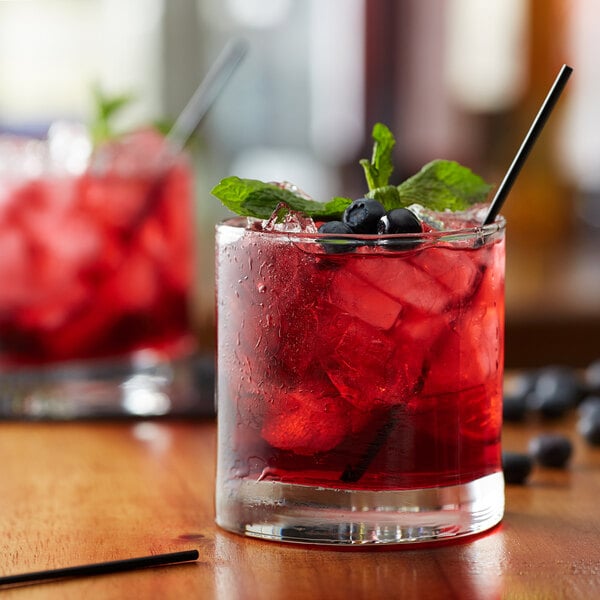 A glass of red Huckleberry flavored drink with ice and berries on a table in a cocktail bar.